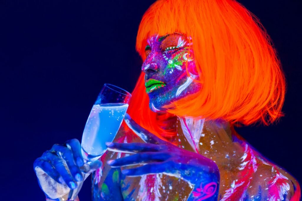 Woman drinking champagne in neon light, disco night club. Beautiful dancer model girl colorful